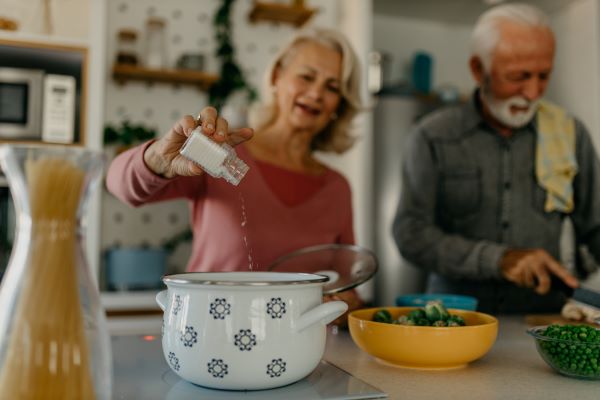 Older adults cooking in the kitchen adding salt to their dish